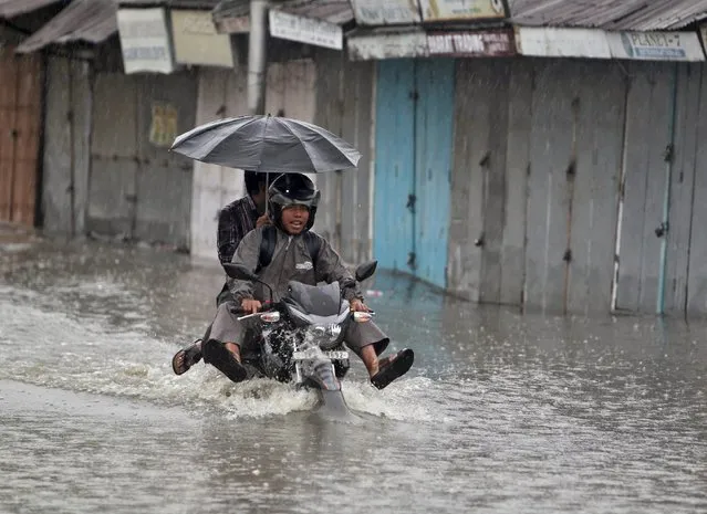 Men ride on a motorcycle through a flooded street during a rain shower in Agartala, India, May 11, 2015. (Photo by Jayanta Dey/Reuters)