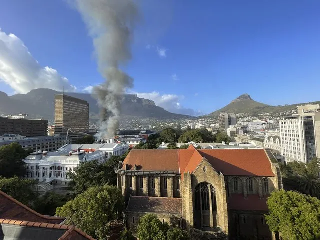 A plume of smoke arises above the Houses of Parliament, behind the St. George's Cathedral, in Cape Town, South Africa, Sunday, January 2, 2022. Firefighters have been deployed and the cause is unknown. (Photo by Jerome Delay/AP Photo)