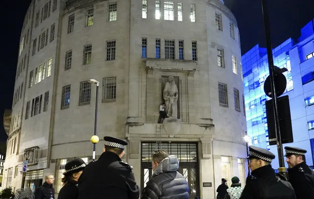 A man, after climbing a ladder, stands next to the statue of Prospero and Ariel from Shakespeare's play The Tempest by the sculptor Eric Gill outside the BBC's Broadcasting House in central London, Wednesday January 12, 2022. British police have cordoned off an area outside the BBC in central London after a man was spotted scaling the building and using a hammer to attack a statue by controversial sculptor Eric Gill. (Photo by Ian West/PA Wire via AP Photo)