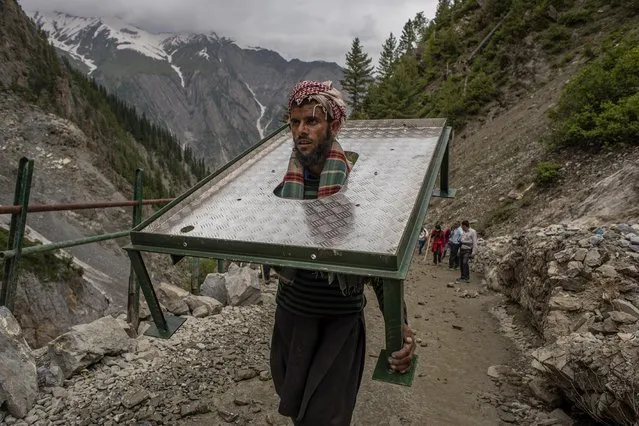 A Kashmiri Muslim laborer carries equipment as he walks towards the sacred Amarnath Cave, one of the most revered of Hindu shrines, on July 1, 2019 in Baltal, 125 km (77 miles) east of Srinagar the summer capital of Indian administered Kashmir, India. Thousands of Hindu devotees, braving sub-zero temperatures, began the hike over glaciers and along paths overhanging gorges to reach the sacred Amarnath cave housing an ice stalagmite, a stylized phallus worshiped by Hindus as a symbol of the god Shiva, surrounded by the Himalayan mountains. More than 200,000 Hindu pilgrims are expected to take part in this year's two month pilgrimage, during which Indian paramilitary soldiers and police are being deployed along the route to protect against attacks by militants who have been fighting for the independence of Kashmir since 1989. Experts and locals say rising temperatures, the activities of the pilgrims such as burning wood and using diesel generators and ferrying pilgrims in choppers to the cave have put a strain on the ecosystem of the area. (Photo by Yawar Nazir/Getty Images)