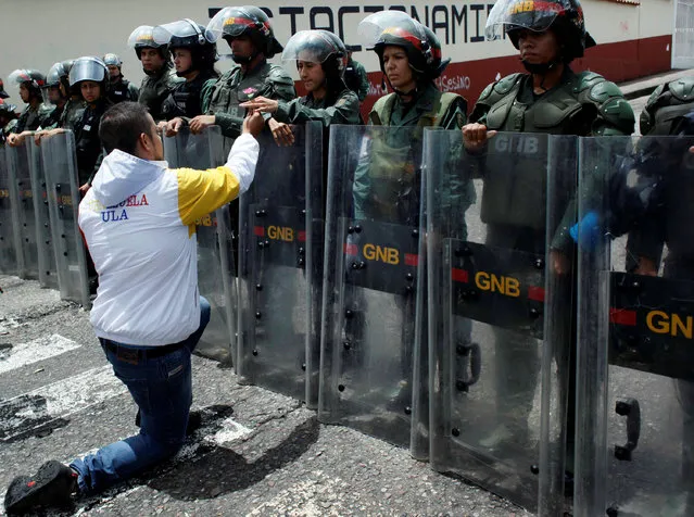 An opposition supporter gives a flower to a Venezuelan National guard, as he kneels during a protest to demand a referendum to remove President Nicolas Maduro in San Cristobal, Venezuela, May 18, 2016. (Photo by Carlos Eduardo Ramirez/Reuters)