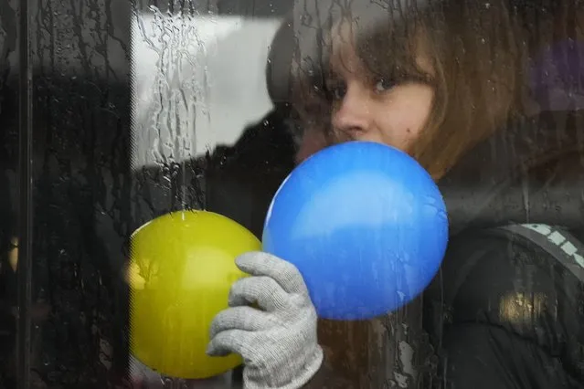 A child looks out from a bus holding balloons in the colours of the Ukrainian flag after fleeing the war from neighbouring Ukraine at the border crossing in Medyka, southeastern Poland, Friday, April 1, 2022. (Photo by Sergei Grits/AP Photo)