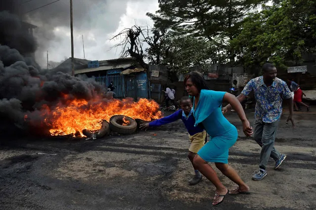 A woman leads a school pupil away from teargas and a burning barricade in Kibera slum, during a demonstration of opposition supporters protesting for a change of leadership ahead of a vote due next years on May 23, 2016 in Nairobi. (Photo by Carl De Souza/AFP Photo)