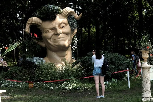 A woman takes a picture of a sculpture depicting servant Puck from Shakespeare's comedy “A Midsummer Night's Dream” during a flower festival in Pakruojis, Lithuania on August 14, 2021. (Photo by Ints Kalnins/Reuters)