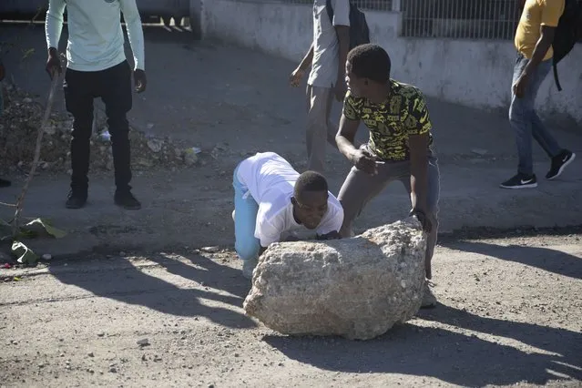 Protesters try to move a chunk of concrete to block a street during a protest by factory workers demanding salary increases in Port-au-Prince, Haiti, Wednesday, February 23, 2022. It is the first day of a three-day strike organized by factory workers who also shut down an industrial park earlier this month to protest pay. (Photo by Joseph Odelyn/AP Photo)