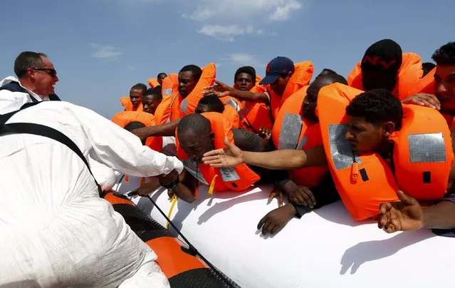 Migrants are helped to cross from their rubber dinghy to a Migrant Offshore Aid Station (MOAS) RHIB (Rigid-hulled inflatable boat) before being taken to the MOAS ship MV Phoenix, some 20 miles (32 kilometres) off the coast of Libya, August 3, 2015. (Photo by Darrin Zammit Lupi/Reuters)
