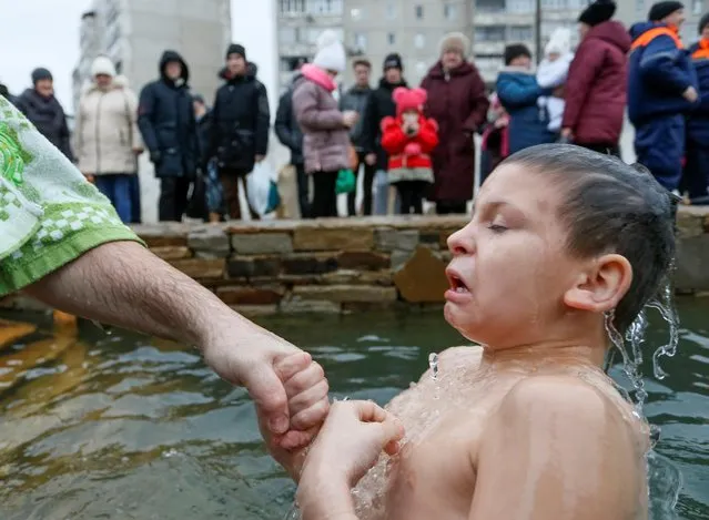 A boy is assisted as he takes a dip during celebrations of the Orthodox Christian feast of Epiphany, in rebel-controlled Luhansk, Ukraine, January 19, 2020. (Photo by Alexander Ermochenko/Reuters)