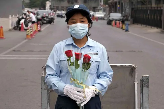 A municipal worker who helped with traffic control near a school is presented with flowers at the end of the national college entrance examinations, known as the gaokao, in Beijing, Friday, June 10, 2022. More than 11 million high school students throughout China took the annual college entrance exams which started on Tuesday after the country has just overcome severe COVID-19 outbreaks in Shanghai and Beijing, according to state media. (Photo by Ng Han Guan/AP Photo)