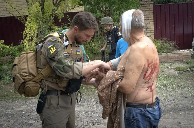 A paramedic helps a man wounded by the Russian shelling at the man's house in Slovyansk, Donetsk region, Ukraine, Thursday, June 30, 2022. (Photo by Efrem Lukatsky/AP Photo)