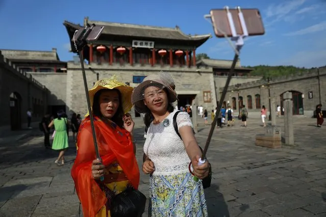 Chinese visitors take selfies with their mobile phones on selfie sticks at the entrance of Gubeishui town at the bottom of the Simatai Great Wall in Miyun county, 120 kilometers northeast of Beijing, China, 23 July 2017. (Photo by How Hwee Young/EPA/EFE)