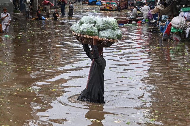 Workers carry vegetables as they wade through a flooded street at a market after a heavy rainfall in Lahore, Pakistan on July 1, 2024. (Photo by Arif Ali/AFP Photo)