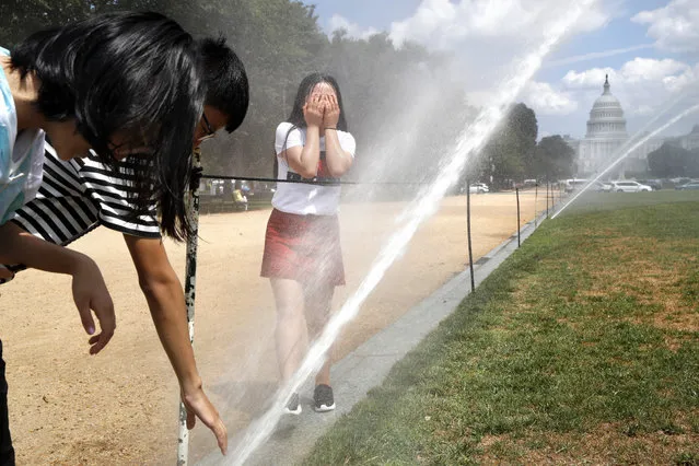 Students visiting from Xining, China, who gave their names as, from left, Maxinya, 14, Lizhengnan, 14, and Lucy, 15, react to the spray coming from large sprinklers watering the lawn of the National Mall as part of turf restoration efforts, Thursday, August 10, 2017, in Washington. (Photo by Jacquelyn Martin/AP Photo)