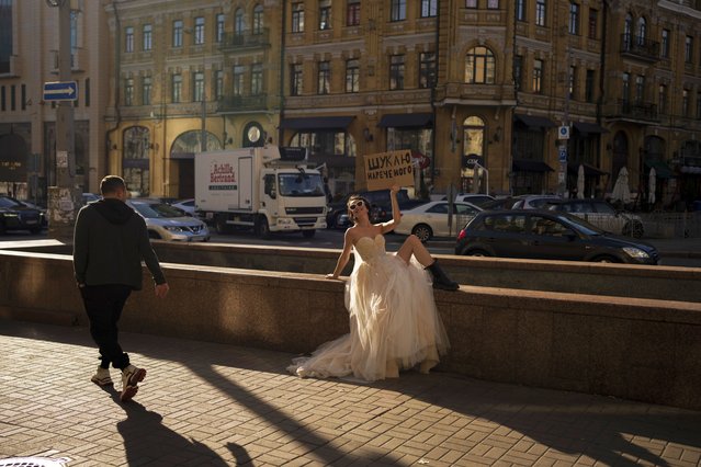 A woman poses for a photograph for a social media campaign in Kyiv, Ukraine, Tuesday, October 31, 2023. The sign reads – “Looking for a groom”. (Photo by Bram Janssen/AP Photo)