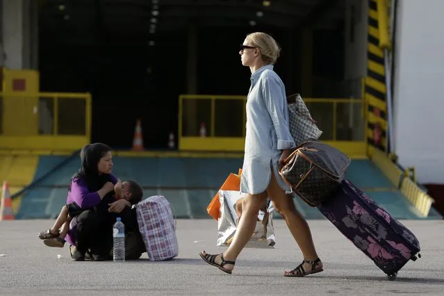 A traveler passes next to an Afghan woman who breastfeeds her baby at the Athens' port of Piraeus on Monday, September 7, 2015. About 2,500 refugees and migrants arrived with the ferry Eleftherios Venizelos as Frontex, the EU border agency, says more than 340,000 asylum seekers have entered the 28-nation bloc this year, the majority fleeing war and human rights abuses in Syria, Afghanistan, Iraq, Somalia and Eritrea. (Photo by Thanassis Stavrakis/AP Photo)