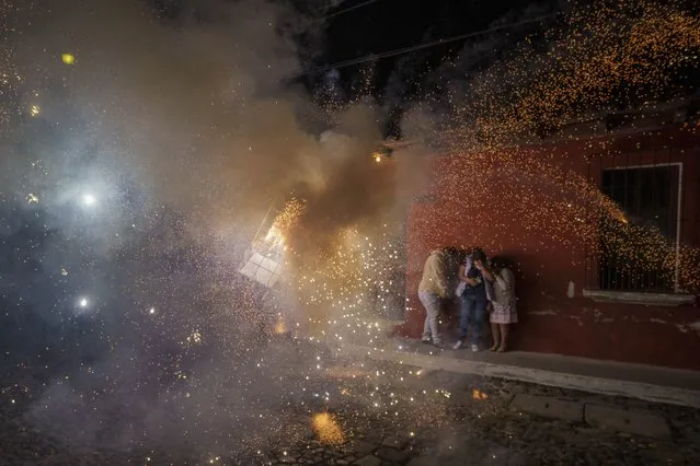 People cover themselves in front of a man wearing a “torito”, a bull-shaped harness equipped with fireworks, during a Christmas celebration in Antigua, Guatemala, late Saturday, December 25, 2021. (Photo by Moises Castillo/AP Photo)