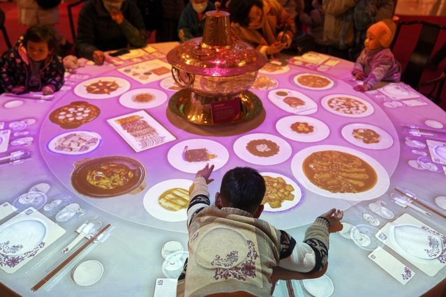 A child reaches to projected dishes on a steamboat table at an exhibition for the upcoming Lunar New Year, in Beijing, Tuesday, January 14, 2025. (Photo by Andy Wong/AP Photo)