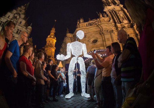 A marionette called “Dundu”, which is handled by five puppet players and is glowing by 250 LED lights, is moved through a crowd of people gathering on the Castle Square in Dresden, Germany, late 20 August 2016, on the occasion of the city's “Stadtfest” festival. (Photo by Arno Burgi/EPA)