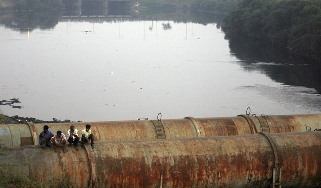 Residents of a slum sit on water pipes going over the contaminated Mithi River in Mumbai December 16, 2009. (Photo by Arko Datta/Reuters)