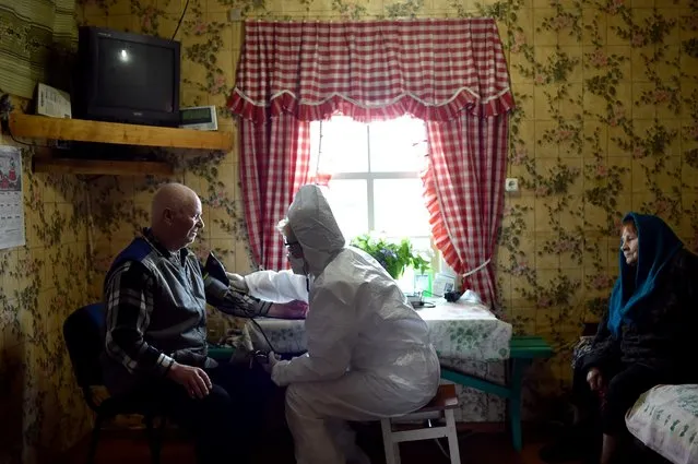 Paramedic Nadezhda Konanava, 65, wearing a protective suit inspects a patient at the village of Novaya Obol, some 70 km outside Vitebsk, on June 1, 2020, amid the COVID-19 pandemic, caused by the novel coronavirus. (Photo by Sergei Gapon/Sputnik/AFP Photo)