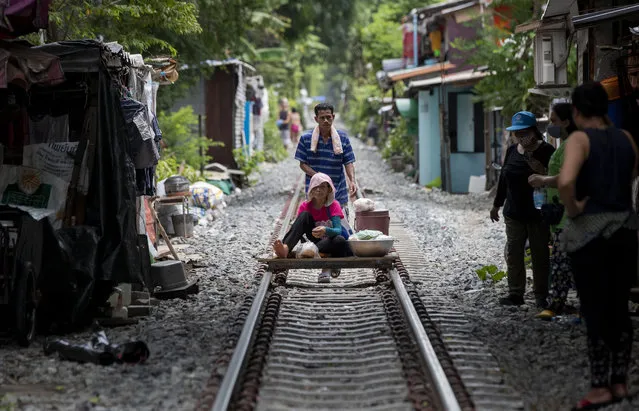 A vendor pushes an improvised cart with a woman and merchandise along a rarely used rail track in Bangkok, Thailand, Thursday, June 25, 2020. Daily life in the capital slowly returns to normal as the Thai government eases many restrictions imposed weeks ago to combat the spread of COVID-19. Though emergency regulations require the use of face masks in public, some residents have become apathetic as Thailand has record zero local transmission for over three weeks. (Photo by Gemunu Amarasinghe/AP Photo)