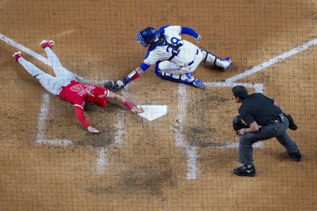 Los Angeles Angels' Kevin Newman, left, slides in to score ahead of the tag by Texas Rangers catcher Jonah Heim, center, as home plate umpire Charlie Ramos looks on on a single by Angels' Luis Rengifo during the sixth inning of a baseball game Wednesday, April 16, 2025, in Arlington, Texas. (Photo by Julio Cortez/AP Photo)