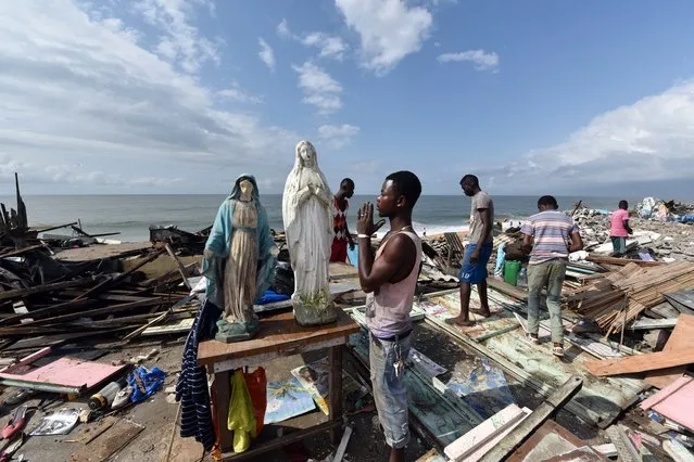 A man prays at the statue of the Virgin Mary amongst the debris of hundreds of destroyed homes, bulldozed during a clean-up operation of the coastal commune of Port Bouet, just east of Abidjan and west of Grand-Bassam, on October 23, 2014. The tearing down of the buildings is part of a clean up operation by the Ivorian government, which also aims to prevent the dangers of the advancing sea. (Photo by Sia Kambou/AFP Photo)