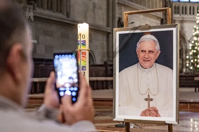 A person takes a picture of a portrait of Pope Emeritus Benedict XVI at St. Peter's Cathedral in Regensburg, Germany, Saturday, December 31, 2022. Pope Emeritus Benedict XVI, the German theologian who will be remembered as the first pope in 600 years to resign, has died, the Vatican announced Saturday. He was 95. (Photo by Armin Weigl/dpa via AP Photo)