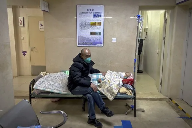 A man wearing a face mask tends to his elderly relative resting in a corridor of the emergency ward to receive an intravenous drip at a hospital in Beijing, Tuesday, January 3, 2023. As the virus continues to rip through China, global organizations and governments have called on the country start sharing data while others have criticized its current numbers as meaningless. (Photo by Andy Wong/AP Photo)