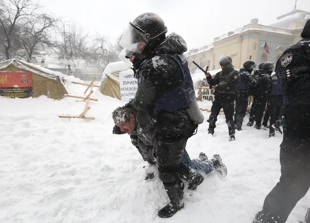 Riot police detain a protester as they assault a tent camp installed by activists of the Movement of New Forces, the political party led by Mikheil Saakashvili, as protesters fire tires in Kiev, Ukraine early Saturday, March 3, 2018. Protesters demand President Petro Poroshenko's impeachment. (Photo by Serhii Nuzhnenko/AP Photo)