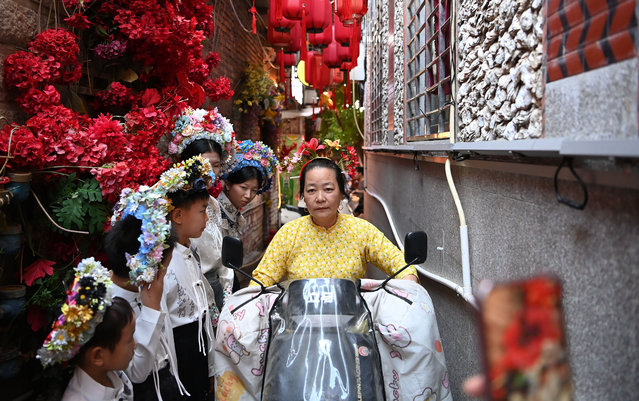 A local woman rides past tourists wearing flowery headwears at Xunpu Village of Quanzhou City, southeast China's Fujian Province, August 18, 2025. Xunpu flowery headwear has been a signature of Xunpu Village and was listed as a national intangible cultural heritage in 2008. The beautiful flowery headwears attracted millions of eyes in the cyber world in early 2023, followed by a sustainable tourist boom in the village. Photo-shooting, dining and other hospitality services have diversified the source of income for residents of this small coastal village that used to rely on fishing and mudflat aquaculture. Since 2025, Xunpu Village has introduced more tourist experience events, such as sea exploration, opera performances, and village sightseeing. These activities have driven the growth of catering, homestays, and related industries, significantly boosting local residents' income. Currently, the village has nearly 300 travel photography studios and receives an average of 20,000 daily tourists. (Photo by Xinhua News Agency/Rex Features/Shutterstock)