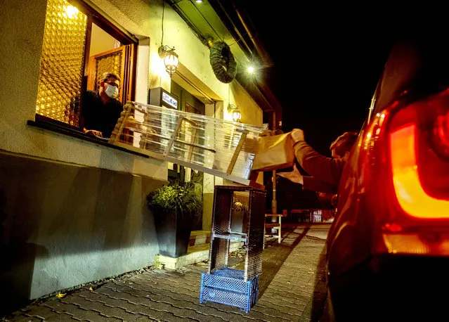In this Thursday, November 5, 2020, a box with food slides down to a car from a window of the apple cider restaurant in “Zum Lahmen Esel” in Frankfurt, Germany. Due to the new partial lockdown to avoid the coronavirus spread the restaurant which has been in operation since 1807 offers cider and food to take-away in a self-made drive through set up. (Photo by Michael Probst/AP Photo/File)