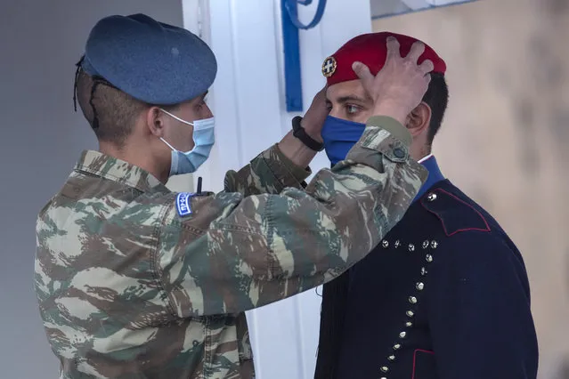 A soldier adjust the attire of a Greek Presidential guard as both they are wearing protective masks against the spread of coronavirus, at the tomb of the unknown soldier, in Athens, on Friday, November 27, 2020. Greece's government spokesman on Thursday announced a weeklong extension to the country's current lockdown, due to the continued spread of the COVID-19. (Photo by Petros Giannakouris/AP Photo)