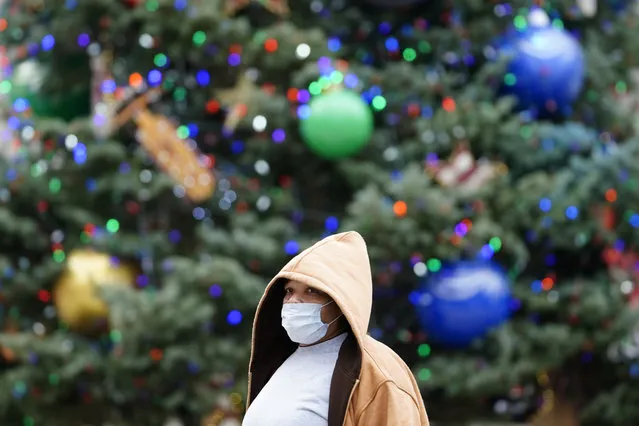 A person wearing a face mask to protect against the spread of the coronavirus walks past holiday decorations at City Hall, Tuesday, December 8, 2020, in Philadelphia. Virtually every state is reporting surges in cases and deaths. (Photo by Matt Slocum/AP Photo)