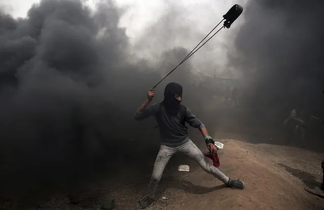 A Palestinian protester hurls stones at Israeli troops during a protest at the Gaza Strip's border with Israel, Friday, April 20, 2018. Thousands of Palestinians joined the fourth weekly protest on Gaza's border with Israel on Friday, some burning tires or flying kites with flaming rags dangling from their tails. Two Palestinians were killed by Israeli troops firing from across the border fence, health officials said. (Photo by Khalil Hamra/AP Photo)