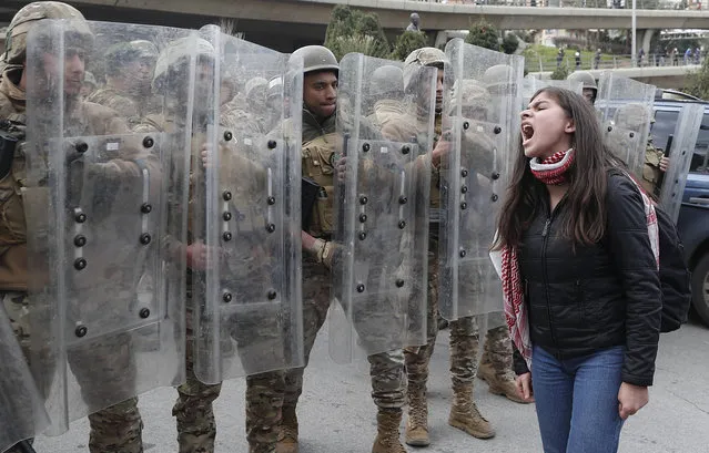 A protester shouts slogans in front of army soldiers during a protest against a parliament session vote of confidence for the new government in downtown Beirut, Lebanon, Tuesday, February 11, 2020. Clashes broke out Tuesday between Lebanese protesters and security forces near the parliament building in central Beirut, where the new Cabinet is scheduled to submit its policy statement ahead of a vote of confidence. (Photo by Hussein Malla/AP Photo)