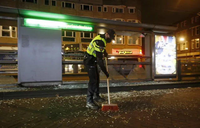 A police officer sweeps up glass from a bus stop that was smashed in protests against a nation-wide curfew in Rotterdam, Netherlands, Monday, January 25, 2021. The Netherlands Saturday entered its toughest phase of anti-coronavirus restrictions to date, imposing a nationwide night-time curfew from 9 p.m. until 4:30 a.m. in a bid to control the COVID-19 infection rate. (Photo by Peter Dejong/AP Photo)