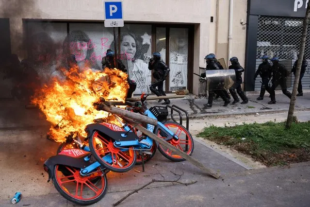French riot police charge past a pile of burning rental bicycles during a demonstration on the 11th day of action after the government pushed a pensions reform through parliament without a vote, using the article 49.3 of the constitution, in Paris on April 6, 2023. France on April 6, 2023 braced for another day of protests and strikes to denounce French President's pension reform one day after talks between the government and unions ended in deadlock. (Photo by Thomas Samson/AFP Photo)