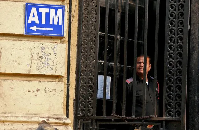 A security guard stands guard outside a branch of the State Bank of india as people gathered to exchange old high denomination bank notes in Old Delhi, India, November 10, 2016. (Photo by Cathal McNaughton/Reuters)