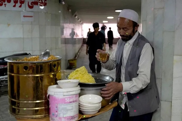 An Afghan vendor selling chickpeas takes a tea break while waiting for customers at an underground walkway in Kabul on June 27, 2023. (Photo by Wakil Kohsar/AFP Photo)