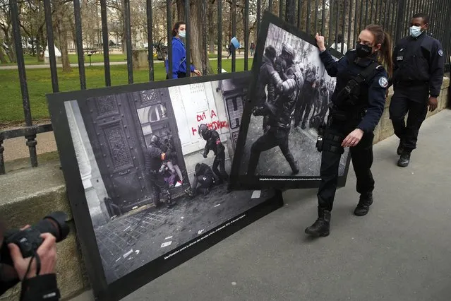 French Police officers remove photos of police violence hung on the fences of the Luxembourg garden next to the Senate during an action of activists from anti-globalization organization ATTAC and Green Peace, to protest against a global security bill in Paris, Thursday, March 18, 2021. Critics protest against a proposed security law they perceive as hardening police tactics and stymieing press freedoms. The government said the measure is needed to better protect police officers from online calls from violence, amid other measures. (Photo by Francois Mori/AP Photo)