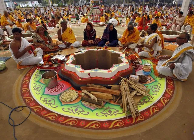 Hindu priests and devotees sit around a decorated "havan kund" or a sacred pit in which fire is lit and offerings are made, as they wait for the start of the prayers on the first day of the five-day long mass prayer meetings for the world peace at a temple on the outskirts of Ahmedabad, India, December 23, 2015. (Photo by Amit Dave/Reuters)