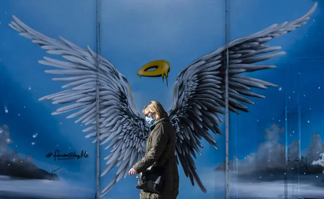 A woman wearing a face mask walks past a mural painting featuring an angel's wings and halo, at a shopping mall in south west Berlin on March 2, 2021, amid the ongoing coronavirus Covid-19 pandemic. Consumer prices in Germany rose at a faster pace in February, preliminary official data showed Monday, as fears grow that a return of inflation could hamper a post-pandemic economic recovery. (Photo by John Macdougall/AFP Photo)