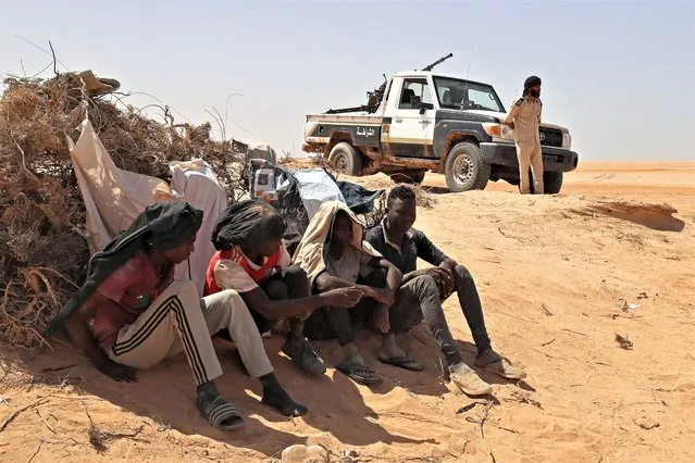 A Libyan border guard stands near migrants from sub-Saharan African countries who claim to have been abandoned in the desert by Tunisian authorities without water or shelter, during a rescue operation in an uninhabited area near the border town of Al-Assah on July 16, 2023. Hundreds of migrants from sub-Saharan African countries were forcibly taken to desert and hostile areas bordering Libya and Algeria after unrest in early July in Sfax, Tunisia's second-largest city. (Photo by Mahmud Turkia/AFP Photo)