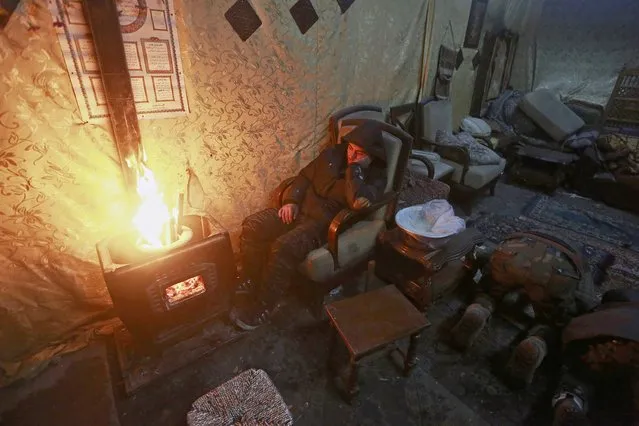 A Free Syrian Army fighter sits next to a fire while a fellow fighter prays inside a safe house on Old Aleppo frontline January 15, 2015. (Photo by Hamid Khatib/Reuters)