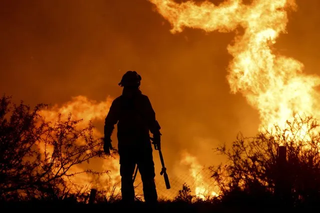 A firefighter is silhouetted by the flames of a forest fire on the outskirts of Villa Carlos Paz, Argentina, Tuesday, October 10, 2023. (Photo by Nicolas Aguilera/AP Photo)