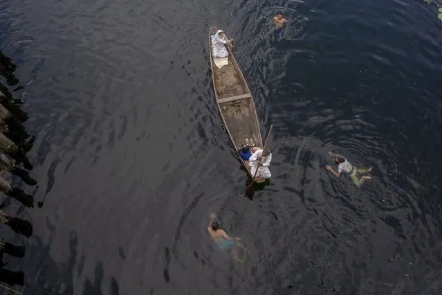 A Kashmiri family row their shikara, or traditional boat, as Kashmiri boys swim in the Nageen Lake on the outskirts of Srinagar, Indian controlled Kashmir, Tuesday, August 3, 2021. Nestled in the Himalayan mountains, Kashmir is known for its beautiful lakes and saucer-shaped valleys. (Photo by Dar Yasin/AP Photo)