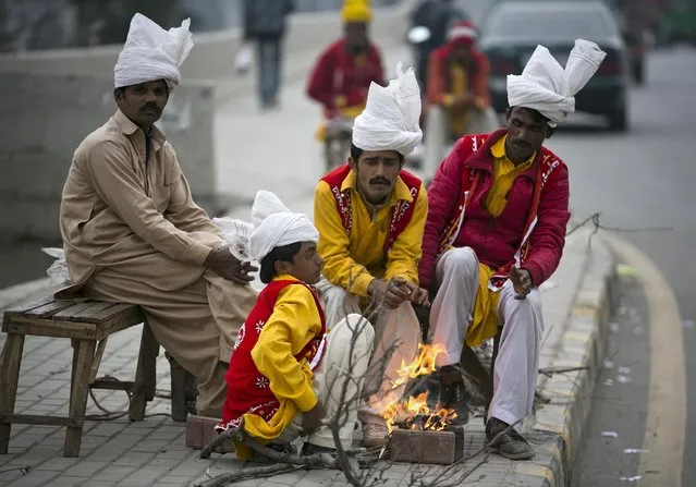 Pakistani street performers sit around fire waiting for customers on a chilly evening in Rawalpindi, Pakistan, Wednesday, February 10, 2016. (Photo by B.K. Bangash/AP Photo)