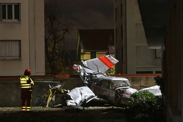 A firefighter stands next to a twin-engined Piper PA-30 Twin Comanche plane after it had to make an emergency landing on a main road and crashed against a wall in downtown Villejuif, a southern Paris' suburb, on December 4, 2023. The plane's three passengers were not seriously injured but admitted to a hospital in a state of shock. (Photo by Miguel Medina/AFP Photo)