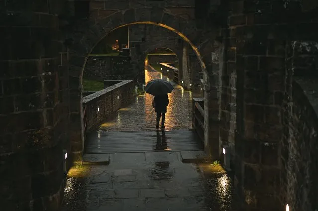 Pedestrian shelters under an umbrella as the rain falls on an autumn evening, in Pamplona, northern Spain, Tuesday, November 21, 2023. (Photo by Alvaro Barrientos/AP Photo)