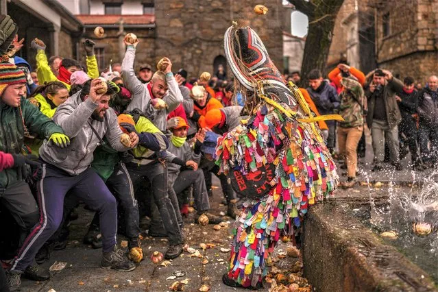 People throw turnips at the Jarramplas as he makes his way through the streets beating his drum during the Jarramplas festival in the tiny southwestern Spanish town of Piornal, Spain, Friday, January 20, 2023. The Jarramplas festival features a man in multicolored garb and pointy wooden headgear to shield himself from turnips. A crowd of men in the street pelt the man with the vegetables from close range at the fiesta held annually at Piornal, 200 kilometers west of Madrid, over two days. (Photo by Manu Fernandez/AP Photo)